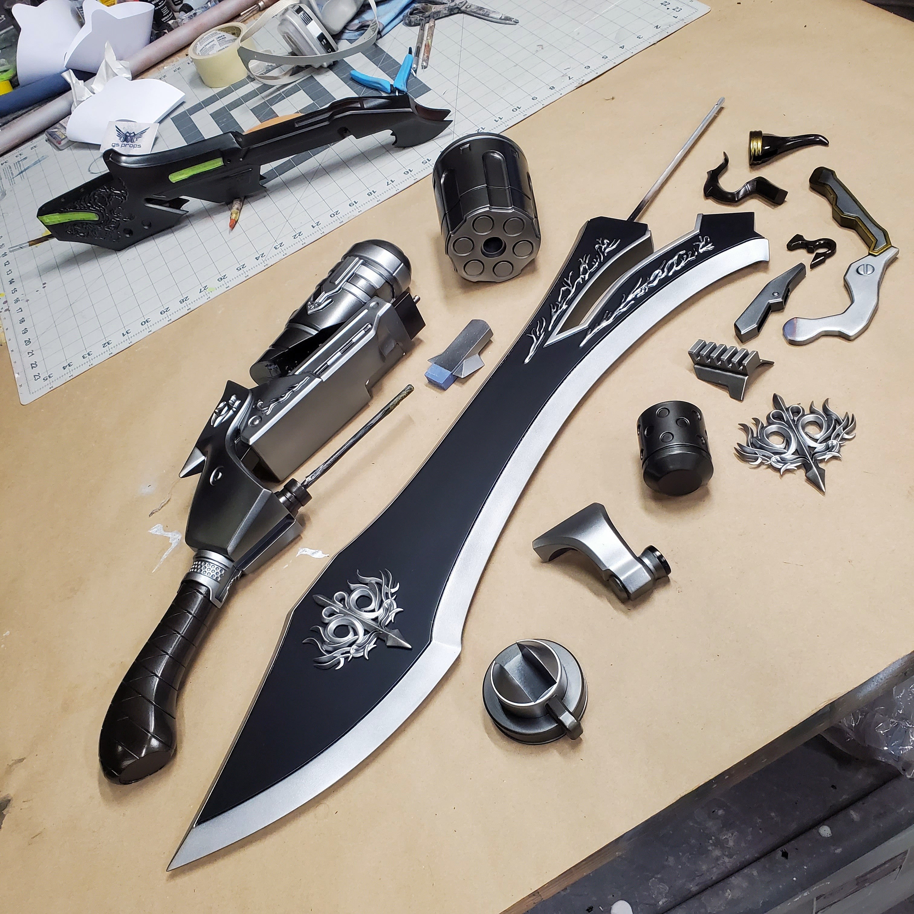 Assorted knife components on a workbench with a large blade and decorative elements.