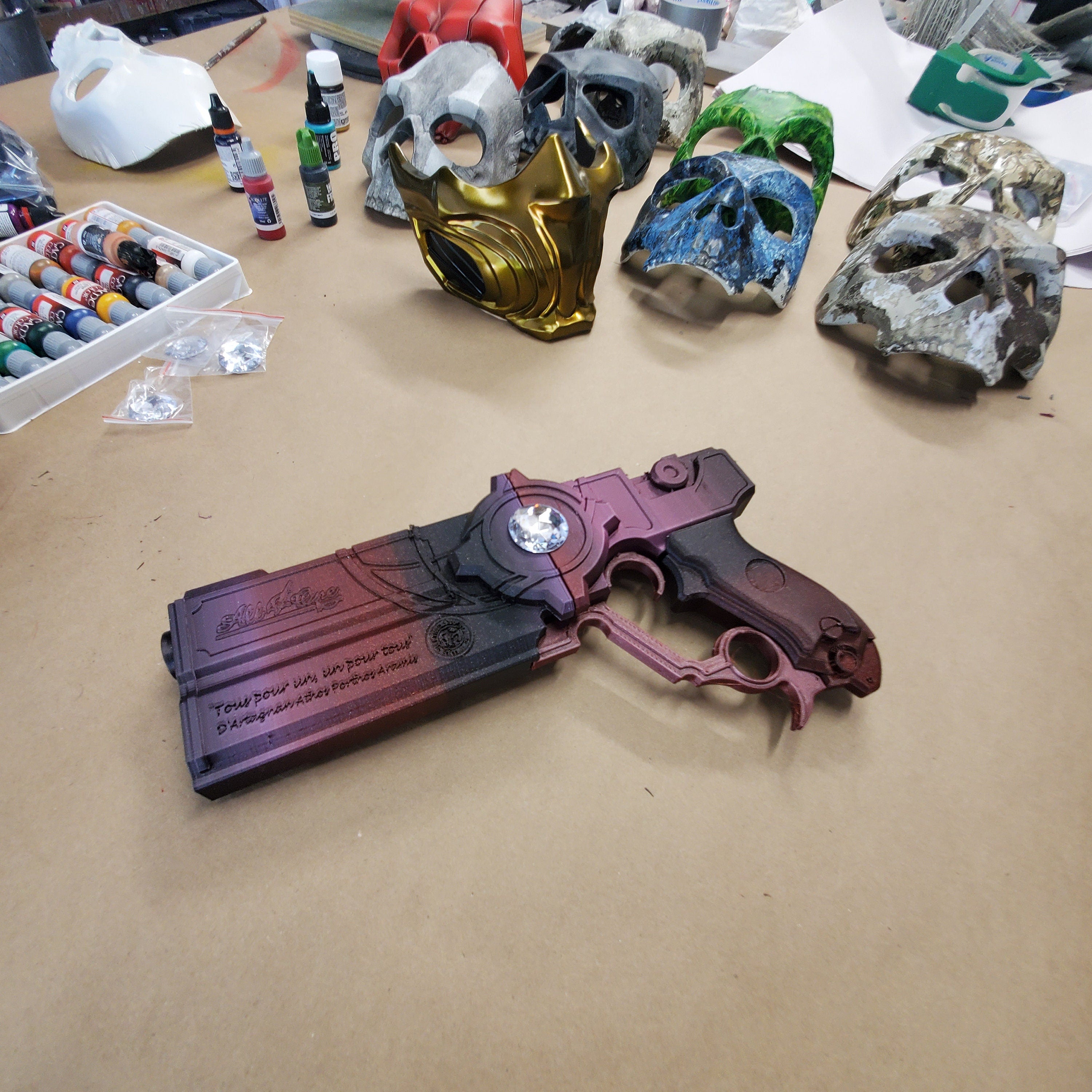 Decorative gun with purple and red design on a table with paint supplies and skull models.