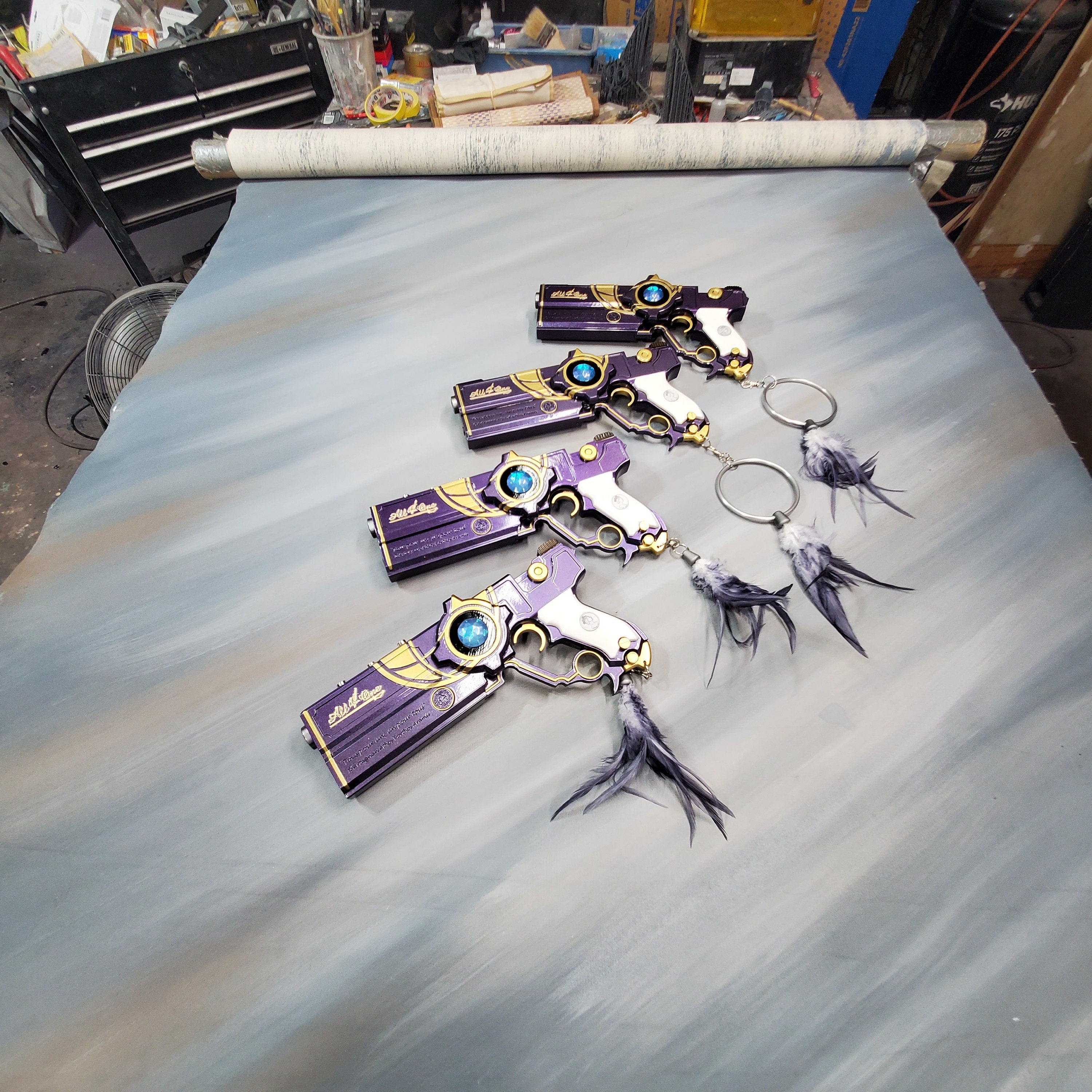 Decorative keychains resembling small guns on a gray surface with tools and materials in the background.